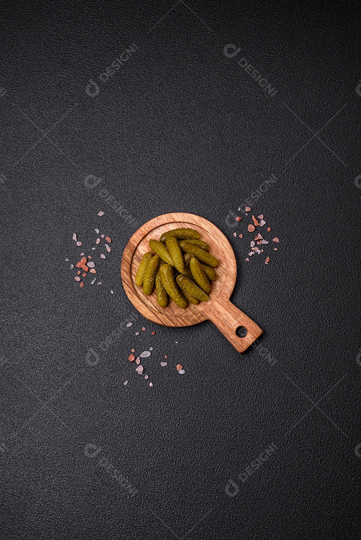 Deliciosos pequenos pepinos em conserva com cebola, mostarda, sal e especiarias sobre um fundo escuro de concreto