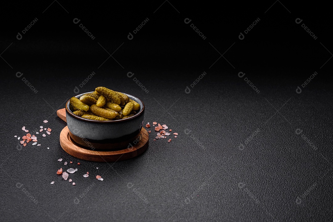 Deliciosos pequenos pepinos em conserva com cebola, mostarda, sal e especiarias sobre um fundo escuro de concreto