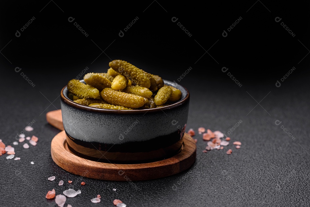 Deliciosos pequenos pepinos em conserva com cebola, mostarda, sal e especiarias sobre um fundo escuro de concreto