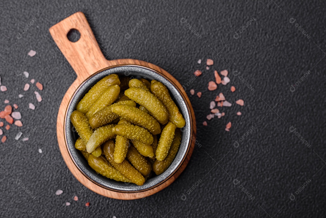 Deliciosos pequenos pepinos em conserva com cebola, mostarda, sal e especiarias sobre um fundo escuro de concreto