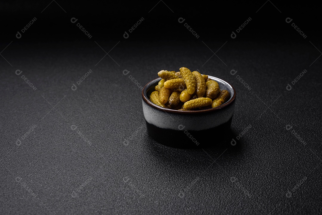 Deliciosos pequenos pepinos em conserva com cebola, mostarda, sal e especiarias sobre um fundo escuro de concreto