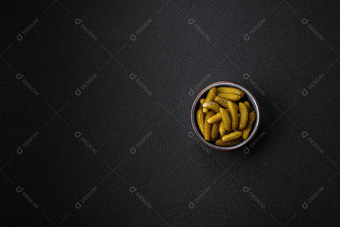 Deliciosos pequenos pepinos em conserva com cebola, mostarda, sal e especiarias sobre um fundo escuro de concreto