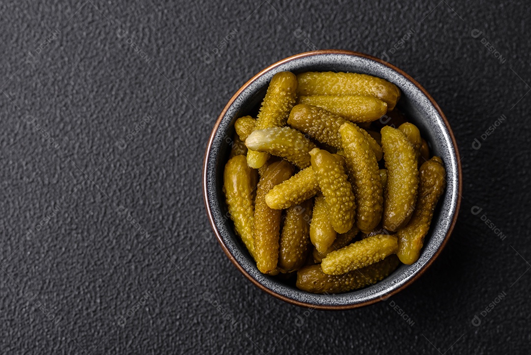 Deliciosos pequenos pepinos em conserva com cebola, mostarda, sal e especiarias sobre um fundo escuro de concreto