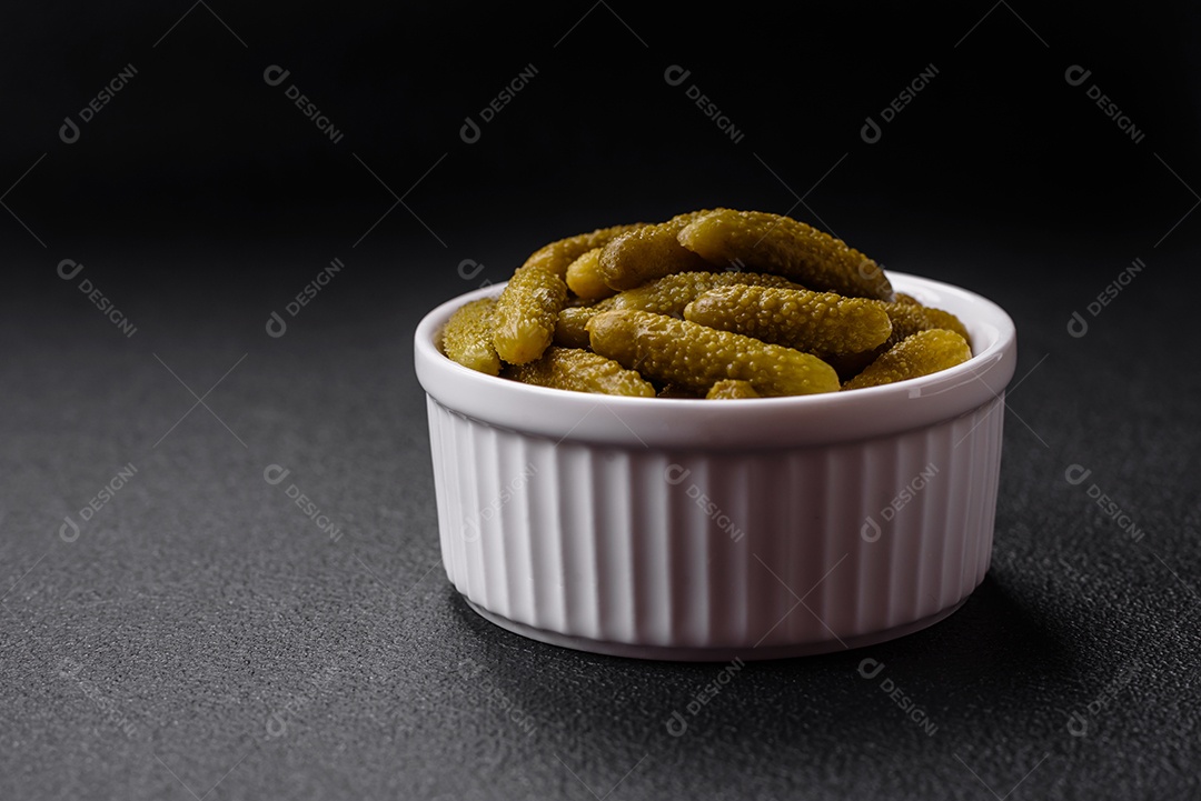 Deliciosos pequenos pepinos em conserva com cebola, mostarda, sal e especiarias sobre um fundo escuro de concreto