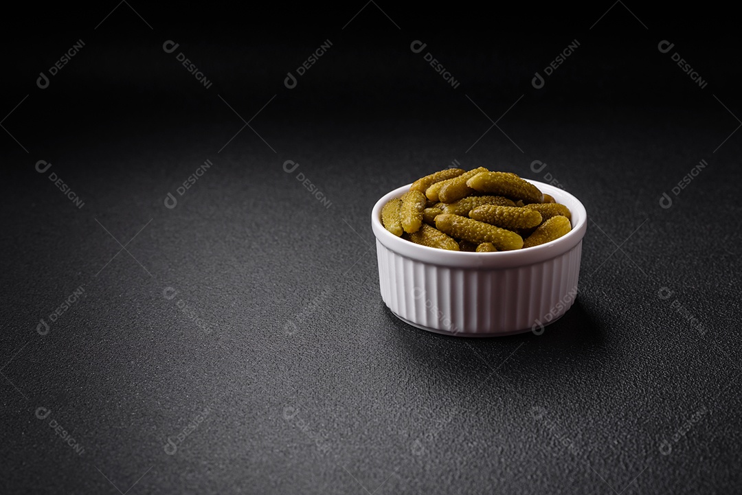 Deliciosos pequenos pepinos em conserva com cebola, mostarda, sal e especiarias sobre um fundo escuro de concreto