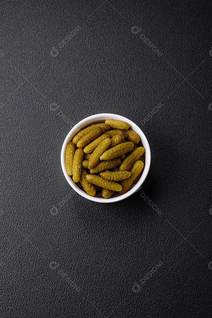 Deliciosos pequenos pepinos em conserva com cebola, mostarda, sal e especiarias sobre um fundo escuro de concreto