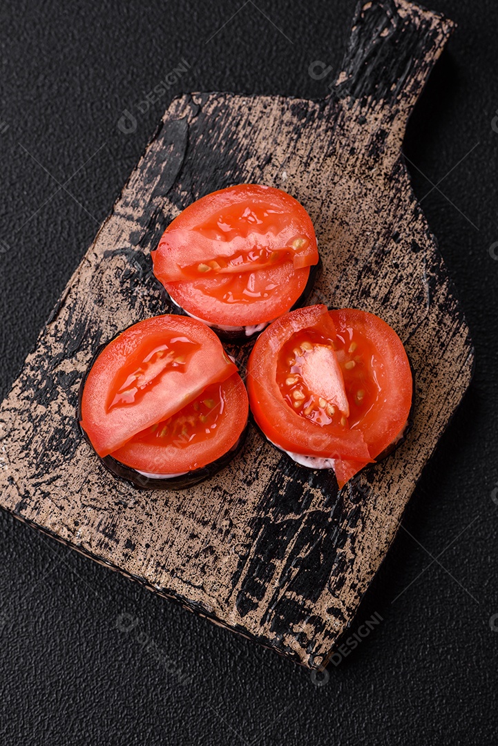 Deliciosa berinjela cortada em círculos grelhada e cozida com maionese e tomate em fundo escuro de concreto