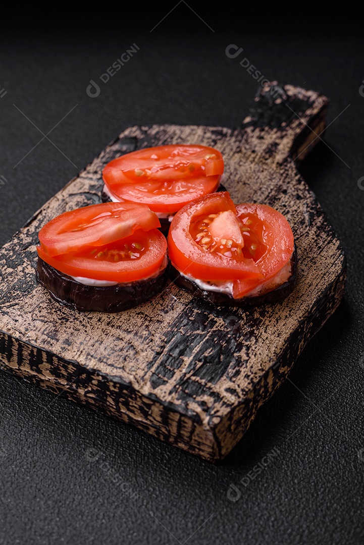 Deliciosa berinjela cortada em círculos grelhada e cozida com maionese e tomate em fundo escuro de concreto
