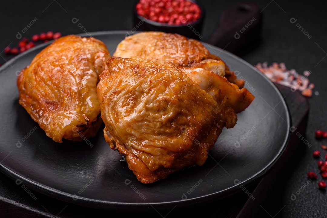 Deliciosas coxas de frango grelhado com sal, especiarias e ervas sobre um fundo escuro de concreto
