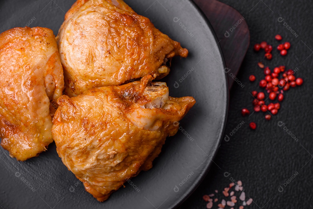 Deliciosas coxas de frango grelhado com sal, especiarias e ervas sobre um fundo escuro de concreto
