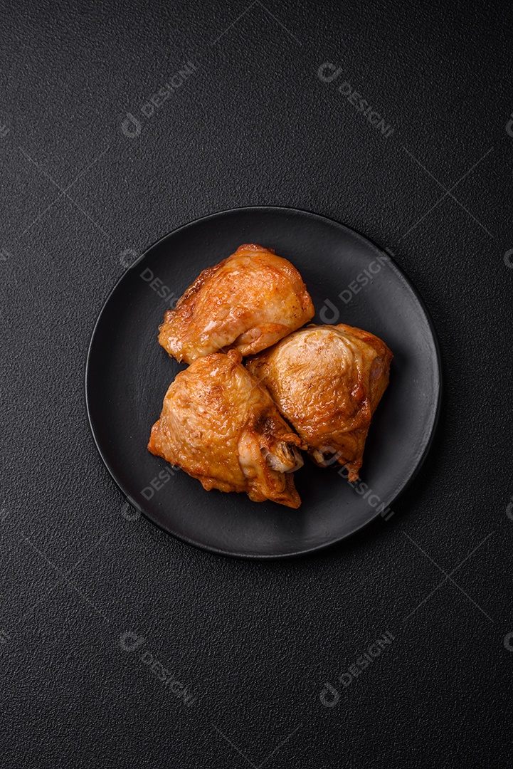 Deliciosas coxas de frango grelhado com sal, especiarias e ervas sobre um fundo escuro de concreto