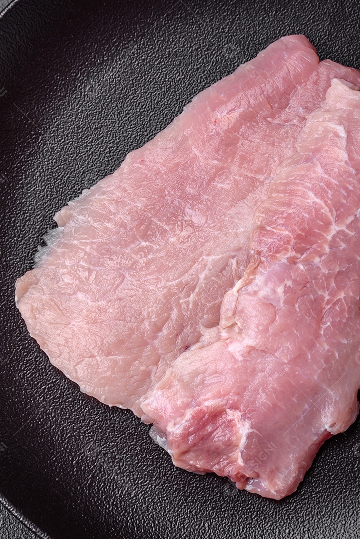 Um pedaço de carne de porco crua fresca e suculenta com sal, especiarias e ervas sobre um fundo escuro de concreto