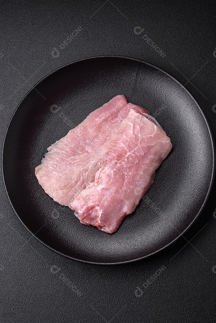 Um pedaço de carne de porco crua fresca e suculenta com sal, especiarias e ervas sobre um fundo escuro de concreto