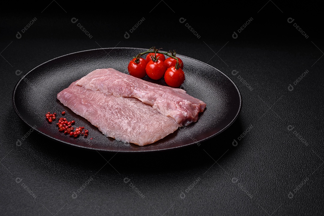 Um pedaço de carne de porco crua fresca e suculenta com sal, especiarias e ervas sobre um fundo escuro de concreto