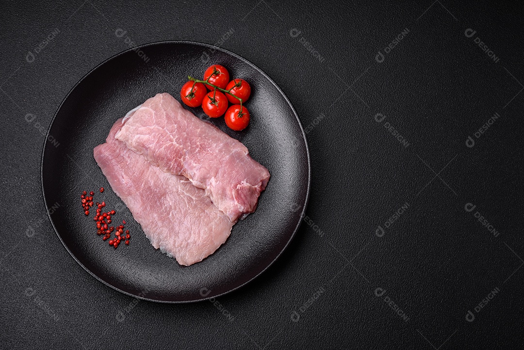 Um pedaço de carne de porco crua fresca e suculenta com sal, especiarias e ervas sobre um fundo escuro de concreto