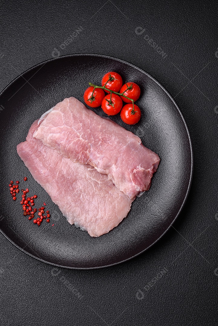 Um pedaço de carne de porco crua fresca e suculenta com sal, especiarias e ervas sobre um fundo escuro de concreto