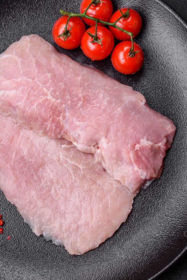 Um pedaço de carne de porco crua fresca e suculenta com sal, especiarias e ervas sobre um fundo escuro de concreto