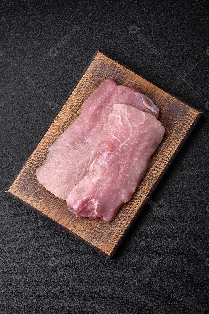 Um pedaço de carne de porco crua fresca e suculenta com sal, especiarias e ervas sobre um fundo escuro de concreto