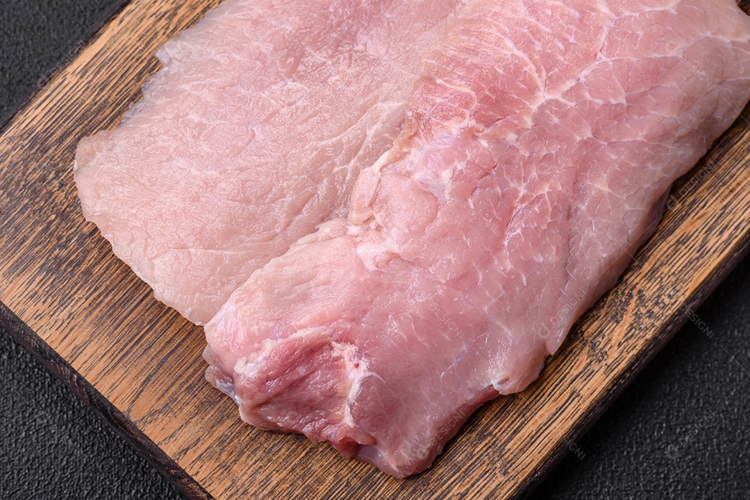 Um pedaço de carne de porco crua fresca e suculenta com sal, especiarias e ervas sobre um fundo escuro de concreto