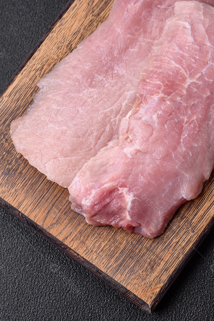 Um pedaço de carne de porco crua fresca e suculenta com sal, especiarias e ervas sobre um fundo escuro de concreto