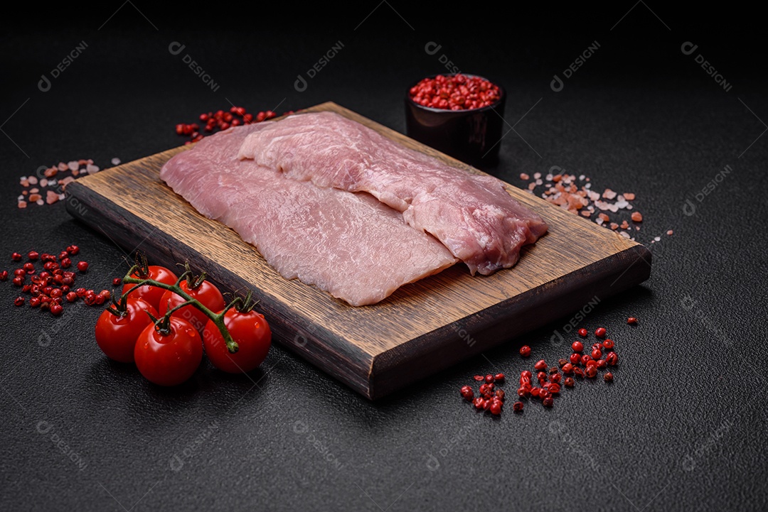 Um pedaço de carne de porco crua fresca e suculenta com sal, especiarias e ervas sobre um fundo escuro de concreto