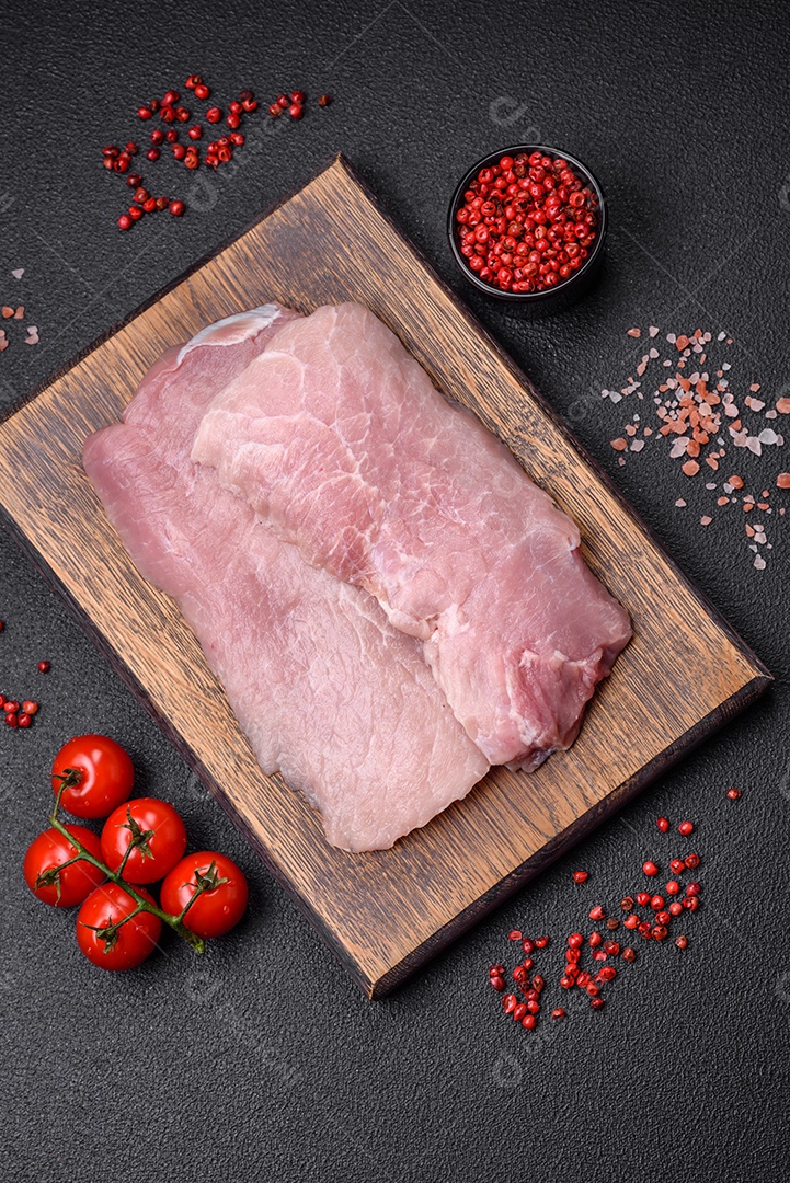Um pedaço de carne de porco crua fresca e suculenta com sal, especiarias e ervas sobre um fundo escuro de concreto