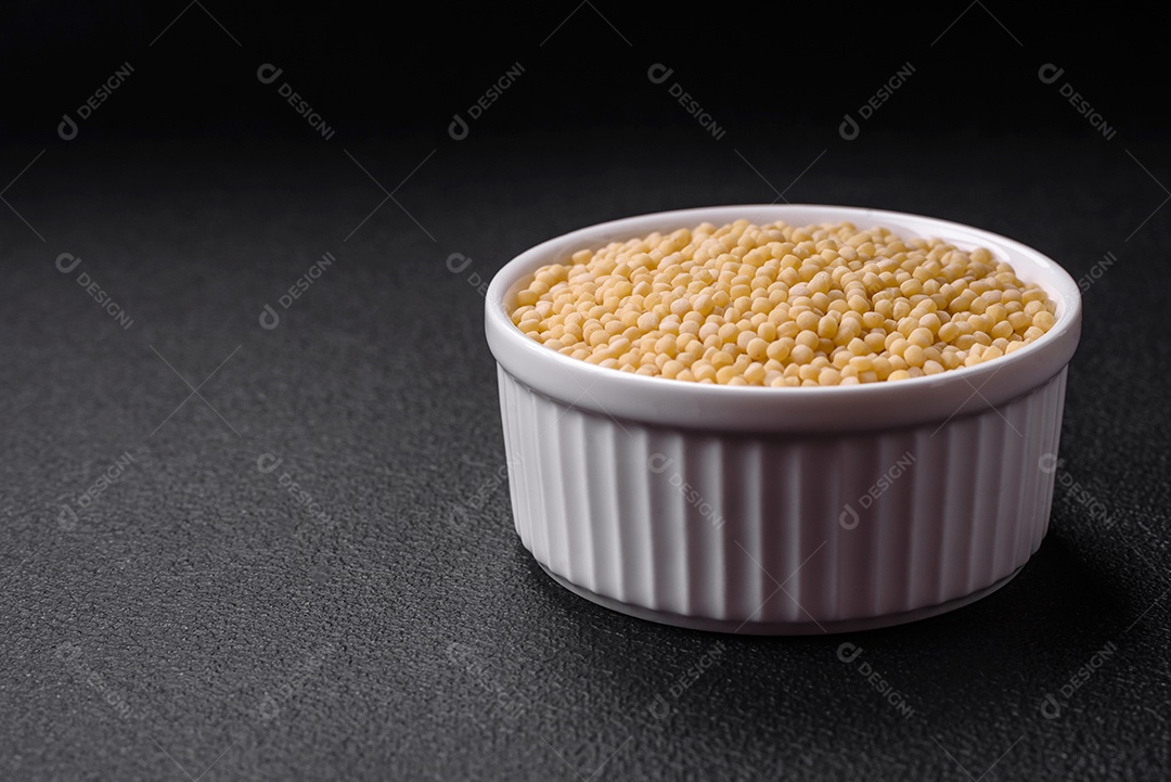 Massa crua ptitim em uma tigela de cerâmica sobre um fundo escuro de concreto. Preparação de comida israelense