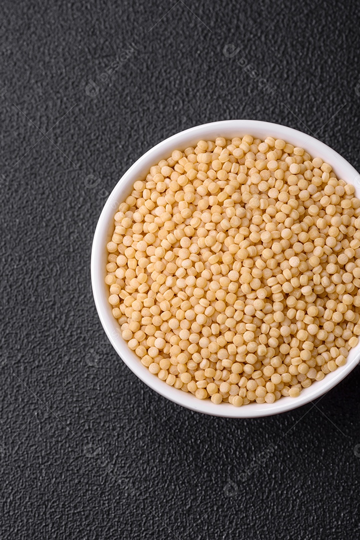 Massa crua ptitim em uma tigela de cerâmica sobre um fundo escuro de concreto. Preparação de comida israelense