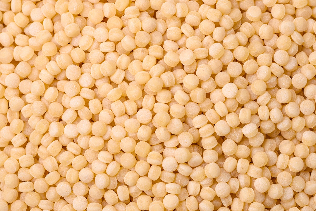 Massa crua ptitim em uma tigela de cerâmica sobre um fundo escuro de concreto. Preparação de comida israelense