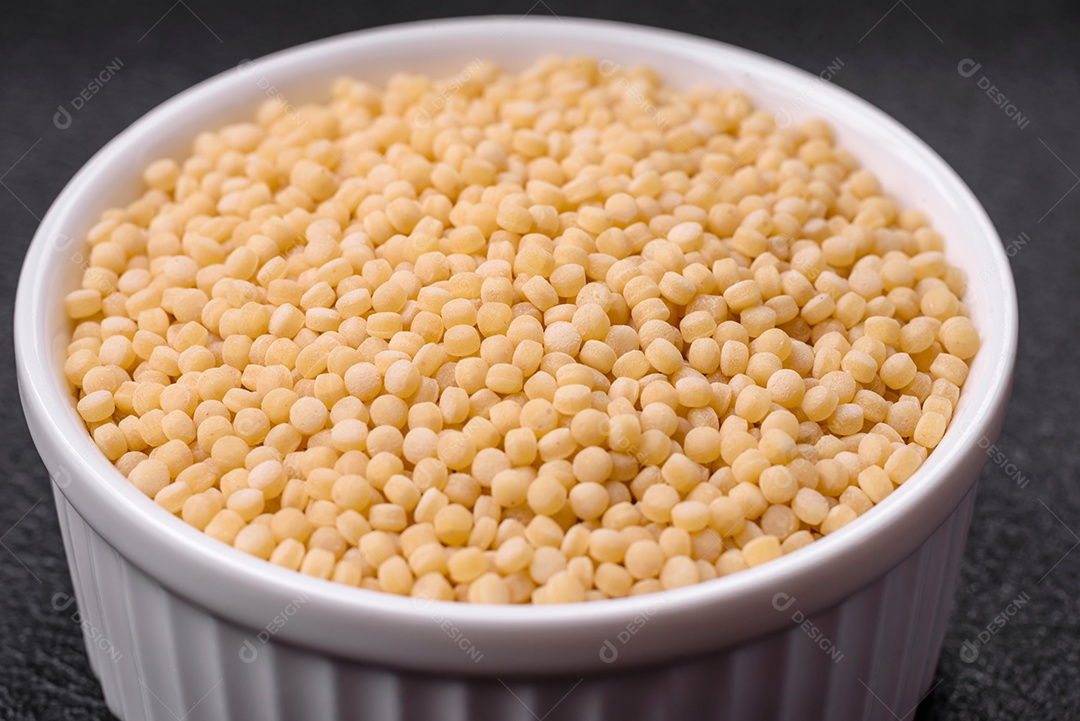 Massa crua ptitim em uma tigela de cerâmica sobre um fundo escuro de concreto. Preparação de comida israelense