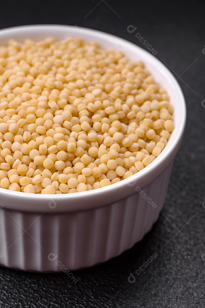 Massa crua ptitim em uma tigela de cerâmica sobre um fundo escuro de concreto. Preparação de comida israelense