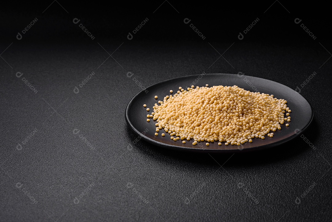 Massa crua ptitim em uma tigela de cerâmica sobre um fundo escuro de concreto. Preparação de comida israelense