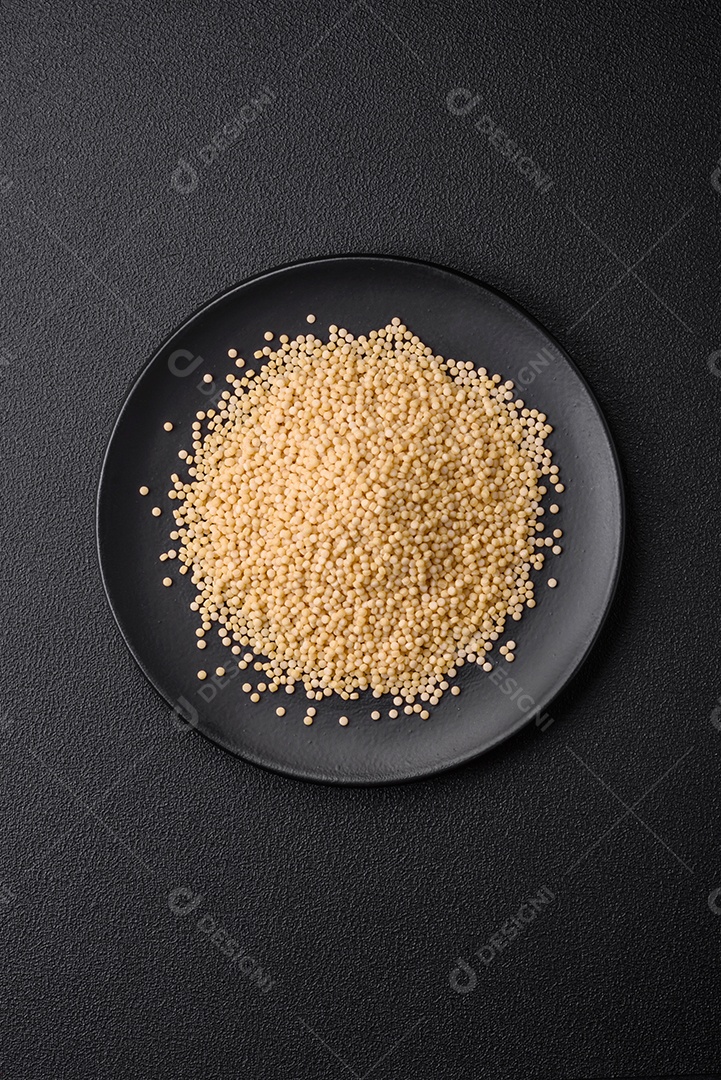 Massa crua ptitim em uma tigela de cerâmica sobre um fundo escuro de concreto. Preparação de comida israelense