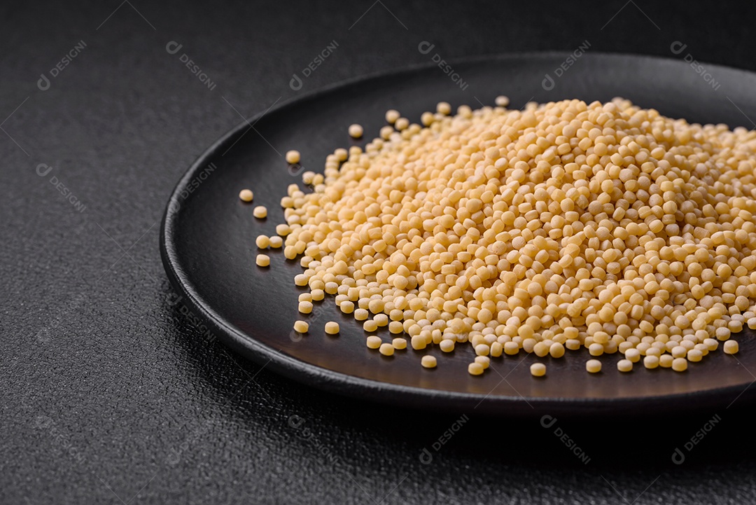 Massa crua ptitim em uma tigela de cerâmica sobre um fundo escuro de concreto. Preparação de comida israelense