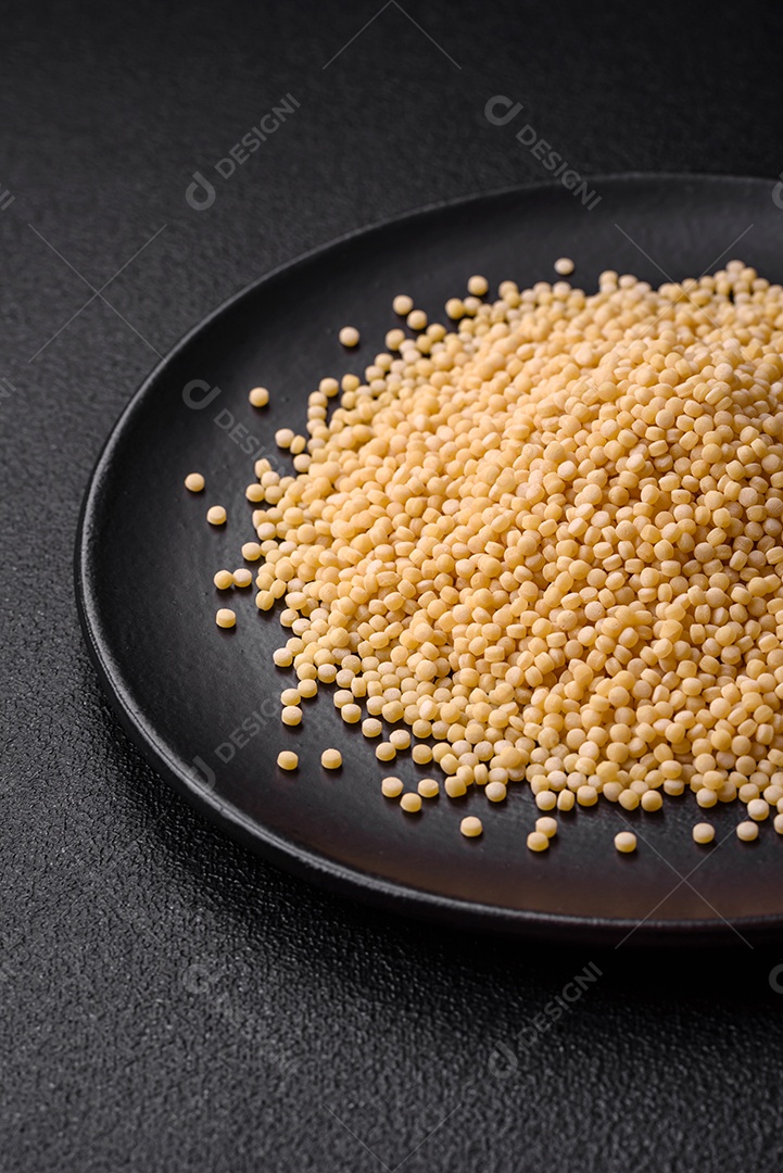 Massa crua ptitim em uma tigela de cerâmica sobre um fundo escuro de concreto. Preparação de comida israelense