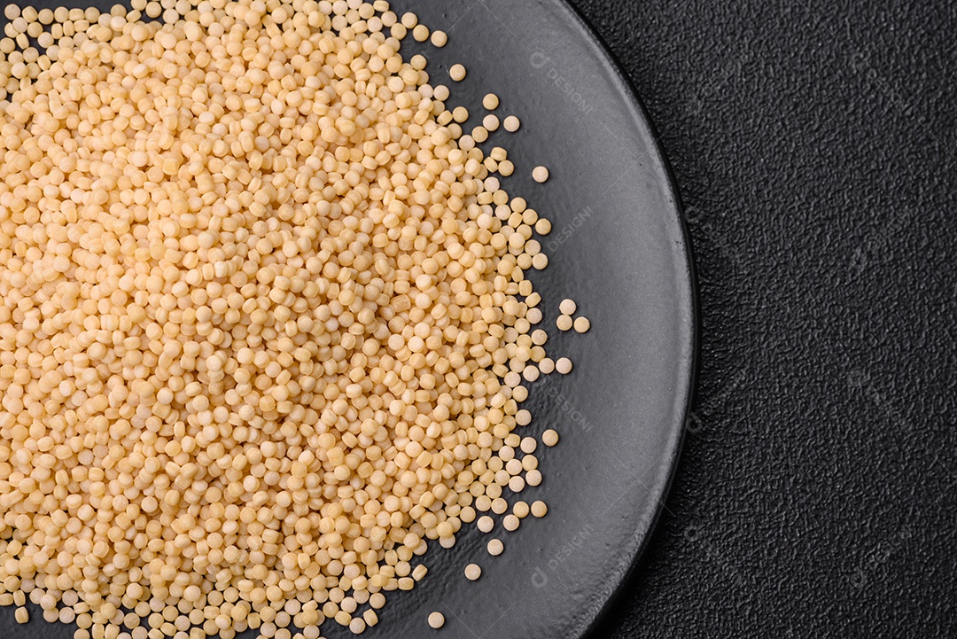 Massa crua ptitim em uma tigela de cerâmica sobre um fundo escuro de concreto. Preparação de comida israelense