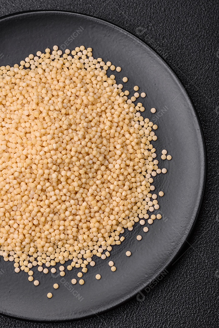 Massa crua ptitim em uma tigela de cerâmica sobre um fundo escuro de concreto. Preparação de comida israelense