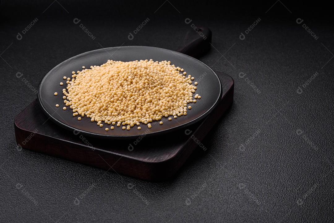 Massa crua ptitim em uma tigela de cerâmica sobre um fundo escuro de concreto. Preparação de comida israelense