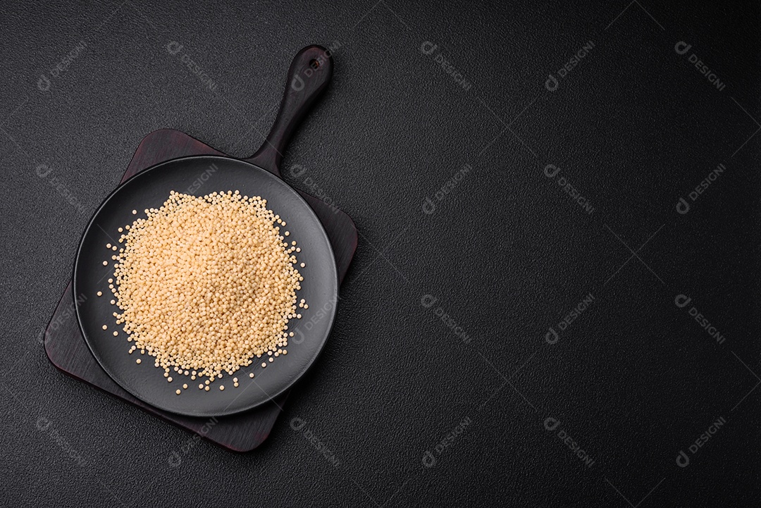 Massa crua ptitim em uma tigela de cerâmica sobre um fundo escuro de concreto. Preparação de comida israelense