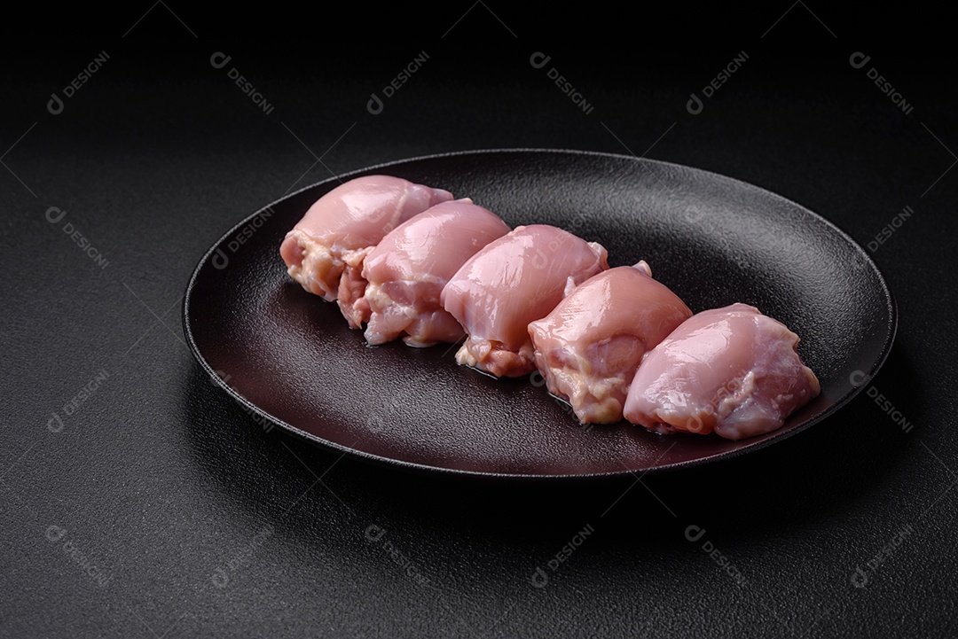 Filetes de coxa de frango cru fresco com sal, especiarias e ervas sobre um fundo escuro de concreto