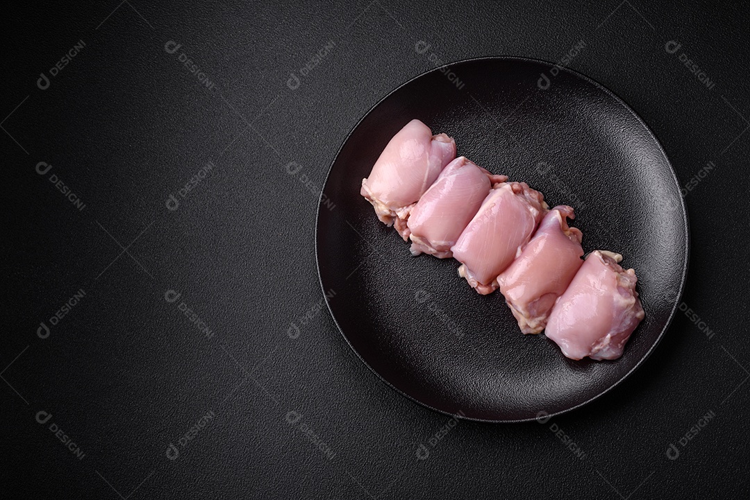 Filetes de coxa de frango cru fresco com sal, especiarias e ervas sobre um fundo escuro de concreto