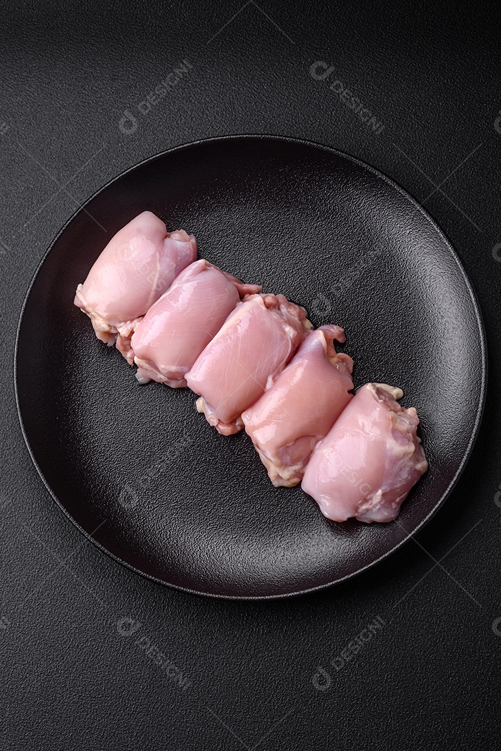 Filetes de coxa de frango cru fresco com sal, especiarias e ervas sobre um fundo escuro de concreto