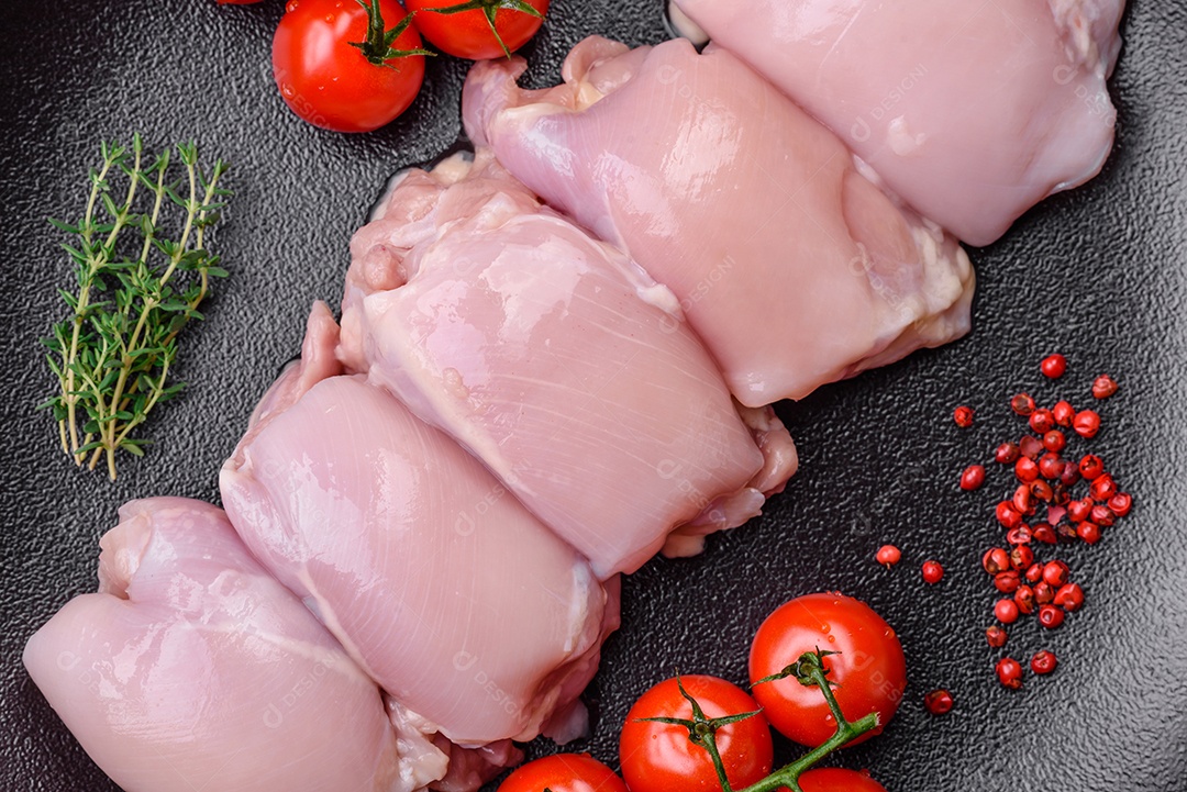 Filetes de coxa de frango cru fresco com sal, especiarias e ervas sobre um fundo escuro de concreto