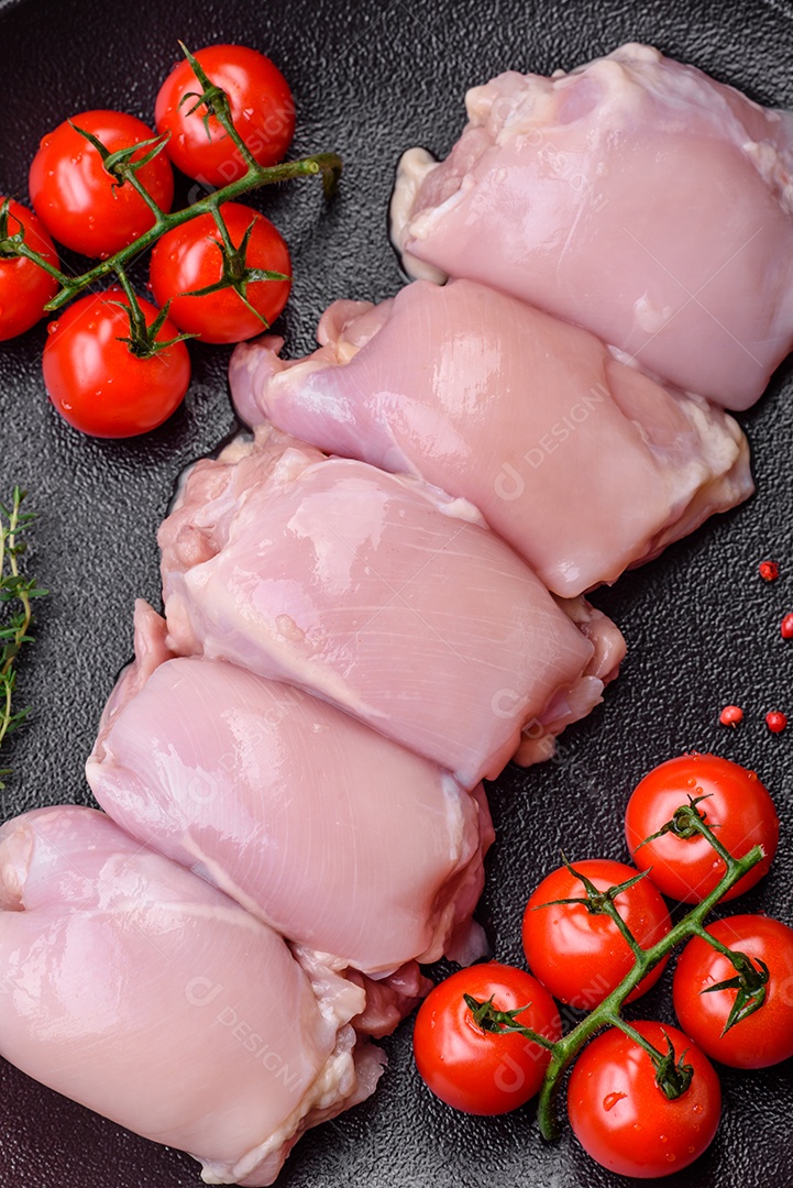 Filetes de coxa de frango cru fresco com sal, especiarias e ervas sobre um fundo escuro de concreto