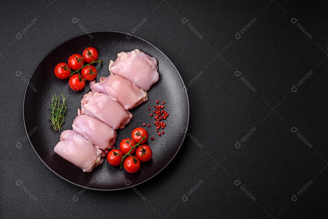 Filetes de coxa de frango cru fresco com sal, especiarias e ervas sobre um fundo escuro de concreto