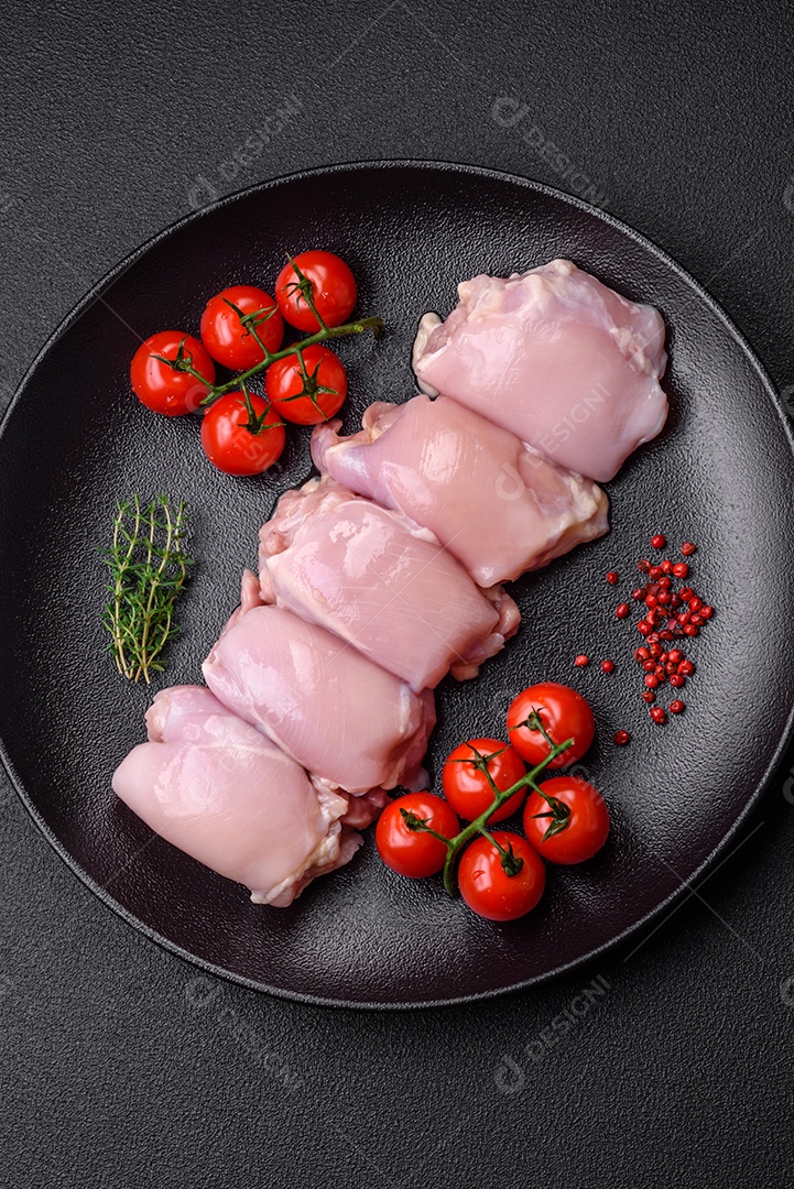 Filetes de coxa de frango cru fresco com sal, especiarias e ervas sobre um fundo escuro de concreto