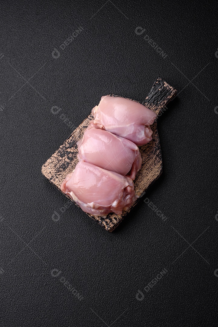 Filetes de coxa de frango cru fresco com sal, especiarias e ervas sobre um fundo escuro de concreto