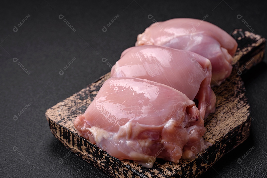 Filetes de coxa de frango cru fresco com sal, especiarias e ervas sobre um fundo escuro de concreto