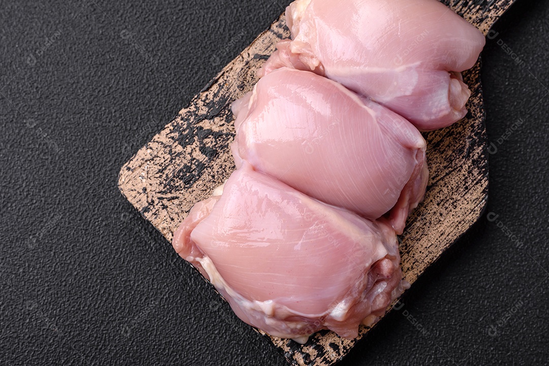 Filetes de coxa de frango cru fresco com sal, especiarias e ervas sobre um fundo escuro de concreto