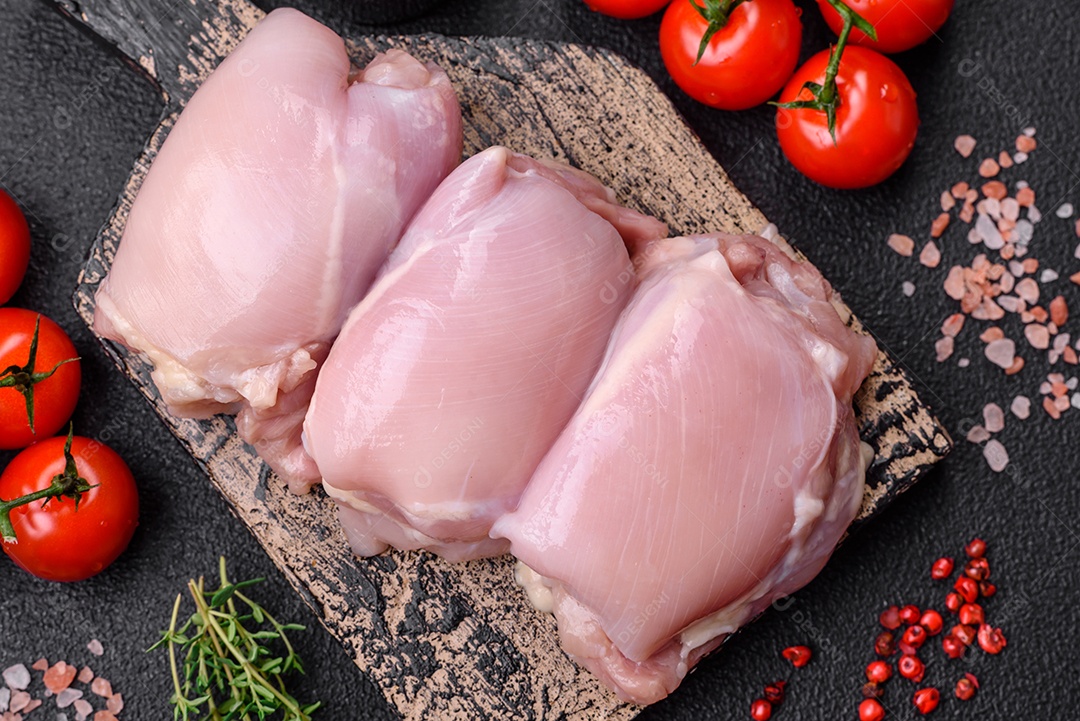 Filetes de coxa de frango cru fresco com sal, especiarias e ervas sobre um fundo escuro de concreto